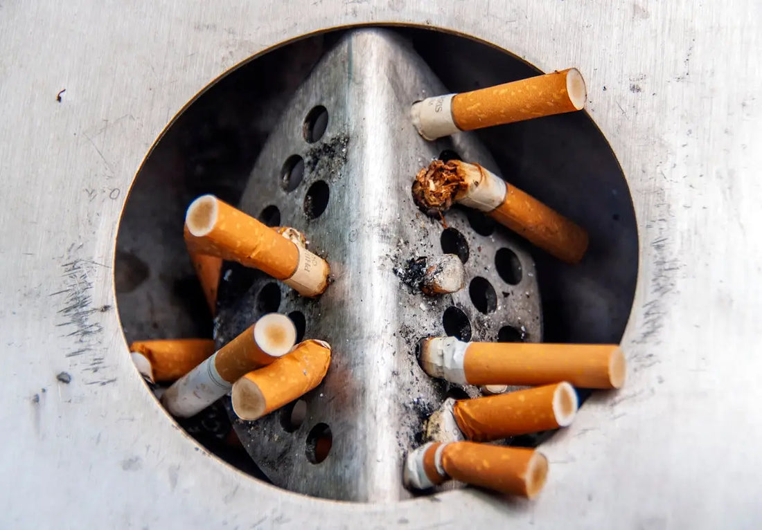 En utomhusbehållare av metall för cigarettavfall fylld med använda fimpar.