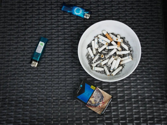 Vit askkopp fylld med cigarettfimpar och aska, svart texturerad bakgrund.