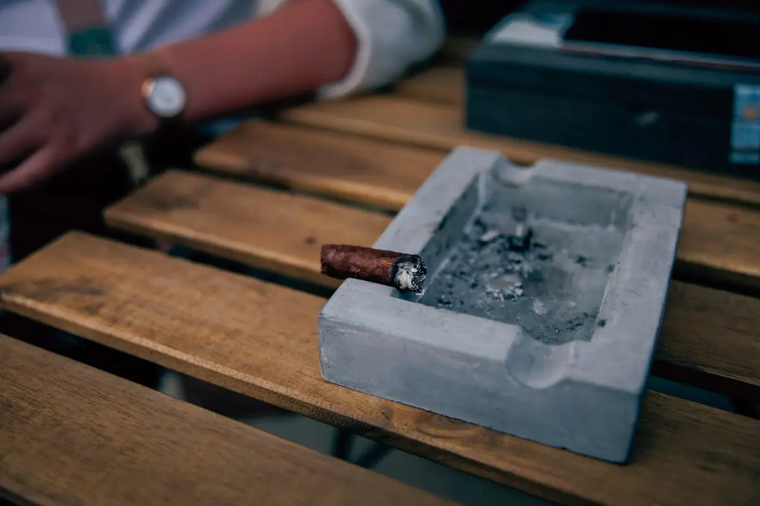 En askkopp i betong med en tänd cigarr.