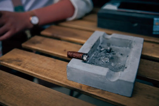 En askkopp i betong med en tänd cigarr.