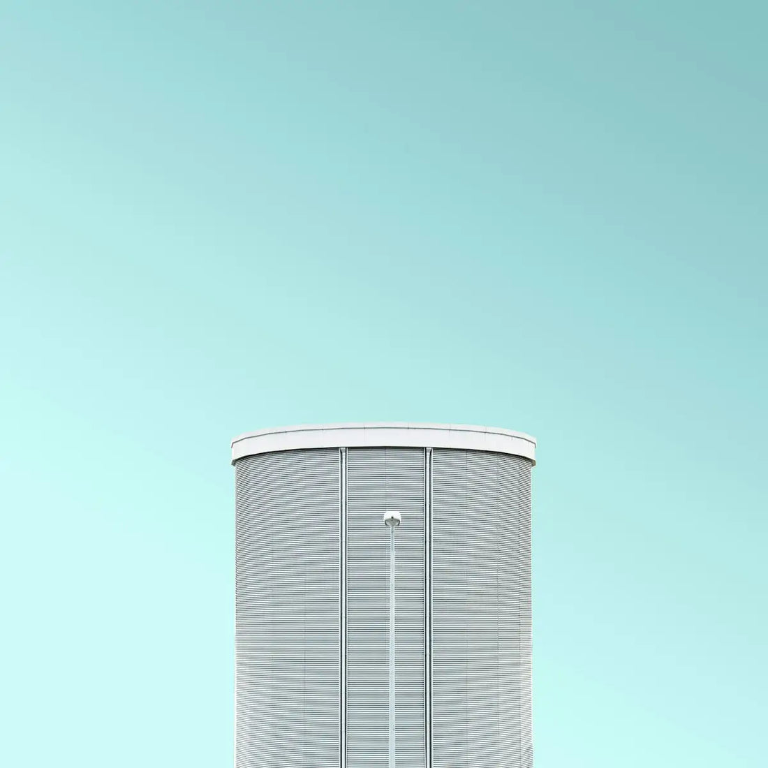 Grå cylindrisk vattentorn med vit list och platt tak.