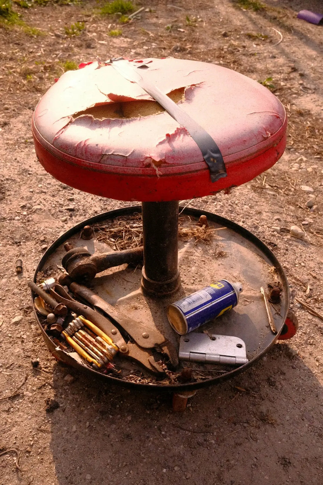 Röd och svart pall med sliten lädersits, metallram och verktyg utspridda på basen.