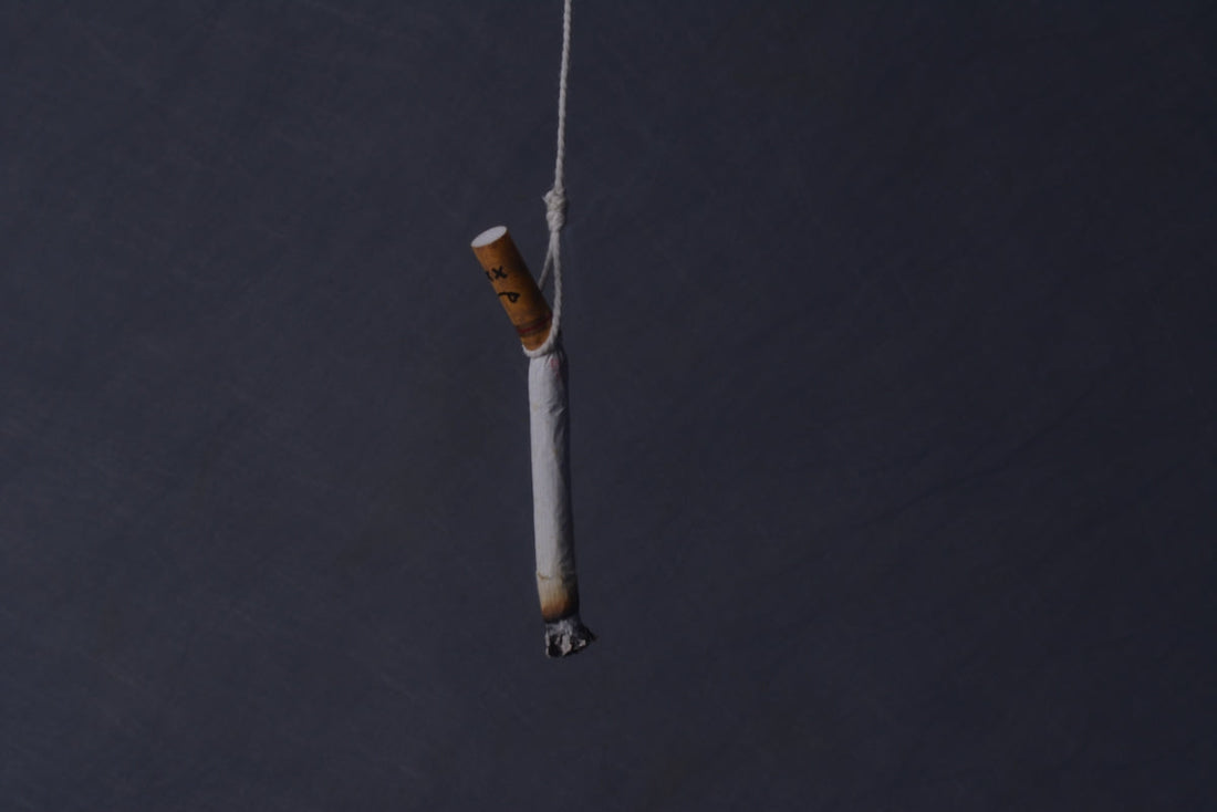 Vit cigarett med aska i spetsen, bunden till ett snöre.