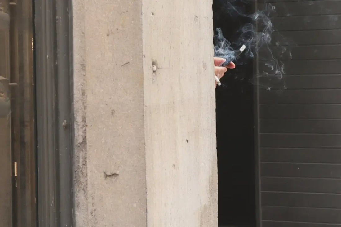 En persons hand som håller i en tänd cigarett med rökutveckling.