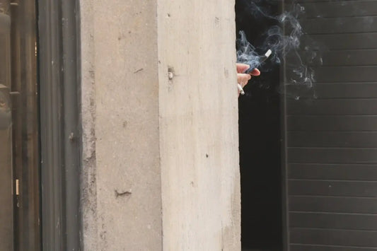 En persons hand som håller i en tänd cigarett med rökutveckling.