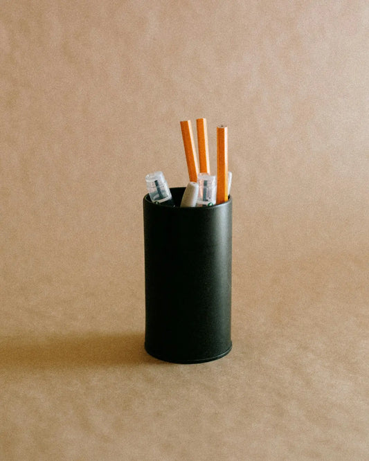 Svart cylindrisk pennhållare med flera orangefärgade pennor och två transparenta pennvässare.